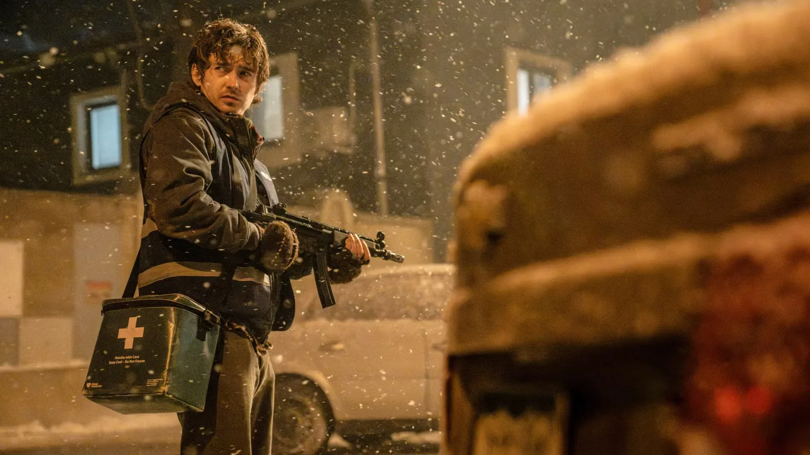 Bryan the medical courier holding a submachine gun and a medical cooler in the snow
