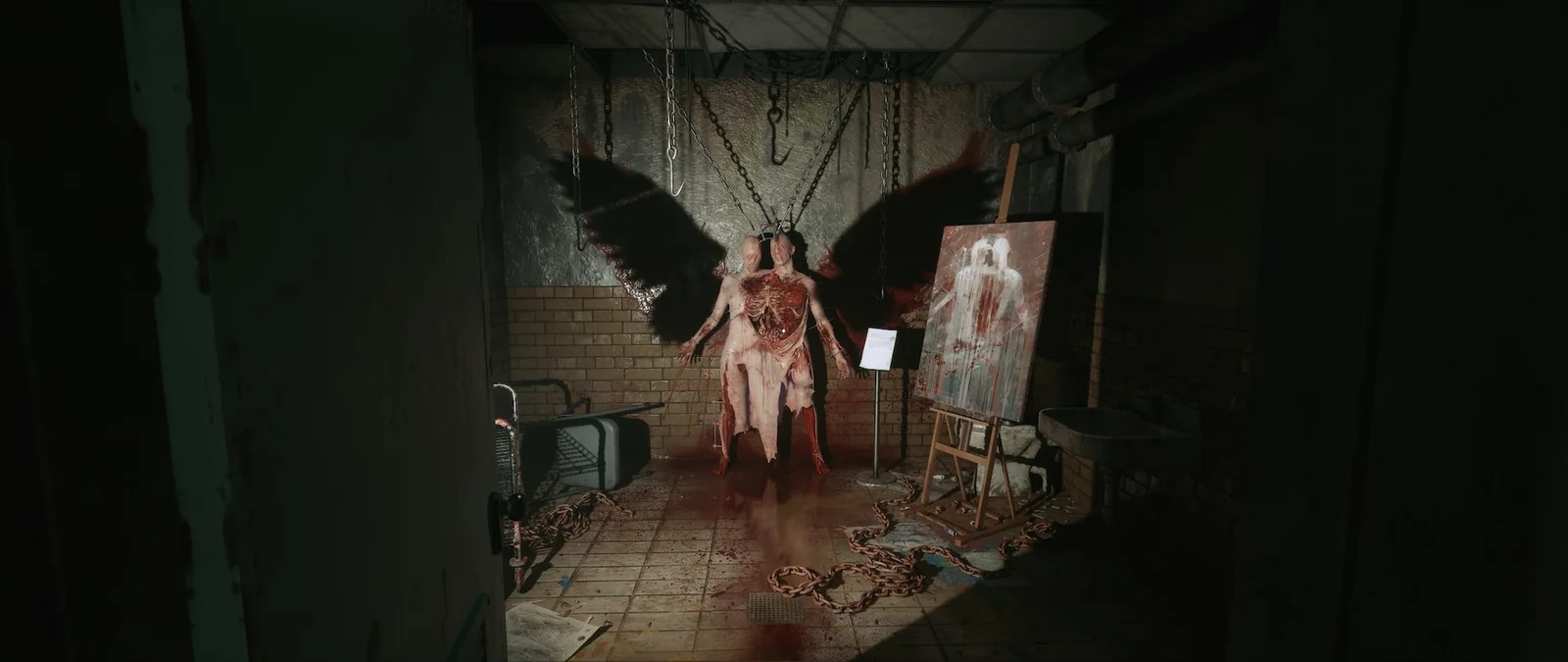 A two-headed, flayed figure with black wings hung on chains in a bloody tiled room, beside a painting of itself on an easel