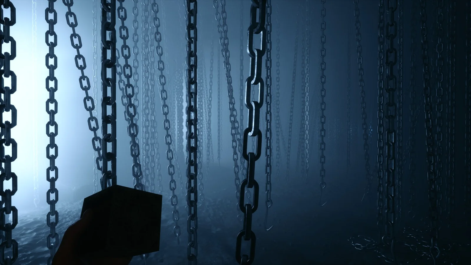 A hand holding the puzzle box in a forest of hanging chains, lit cold blue