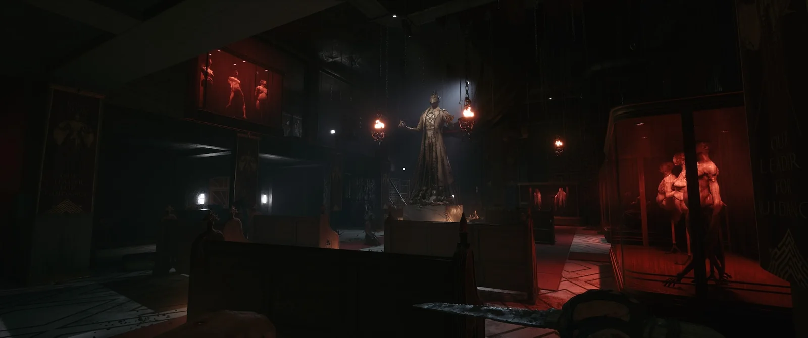 A cult chapel lit red, with wooden pews, a robed statue under a spotlight, and banners reading Our Leader for Guidance