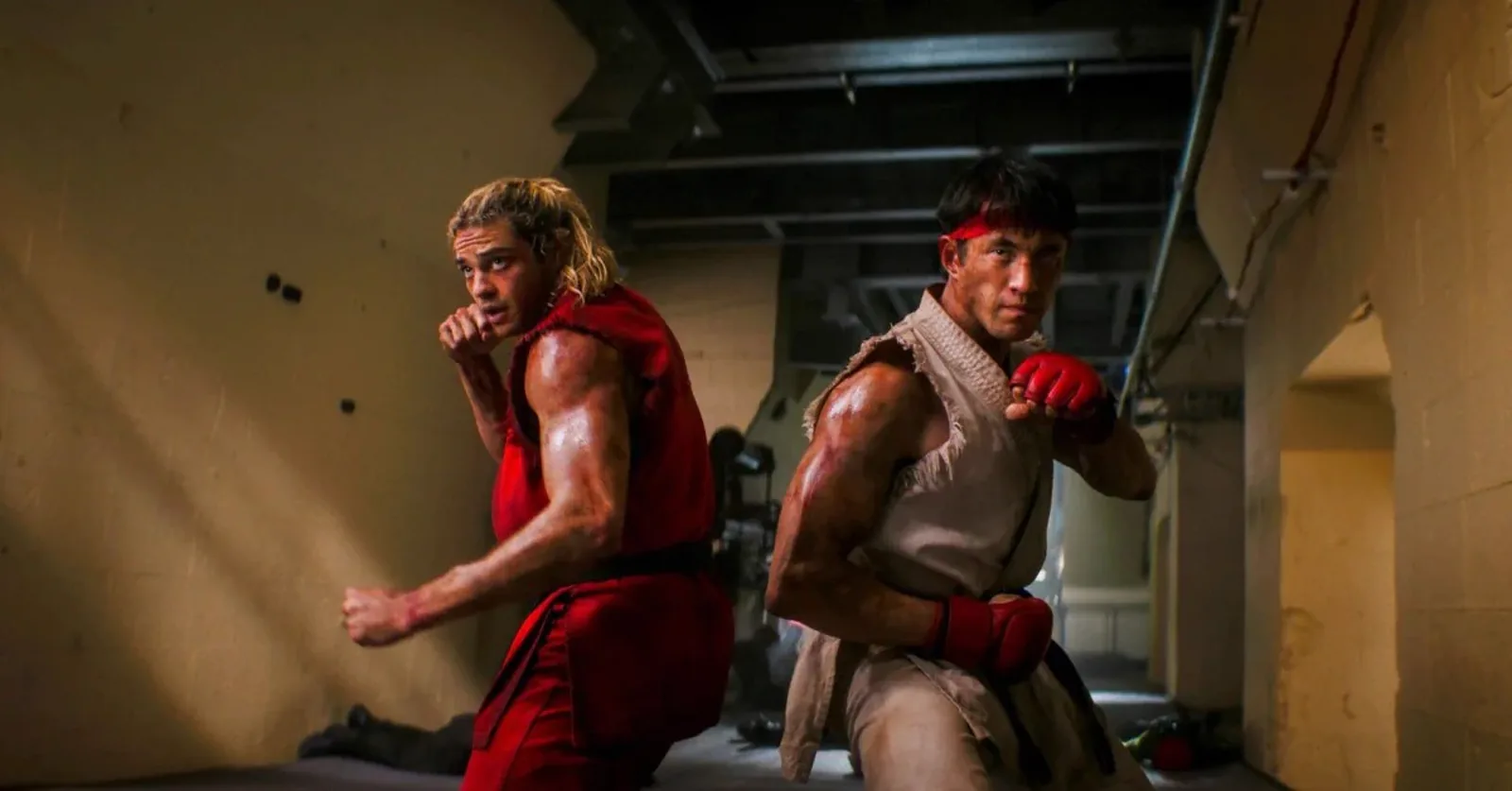 Ken in his red gi and Ryu in his white gi, side by side in their fighting stances in a grimy concrete hallway