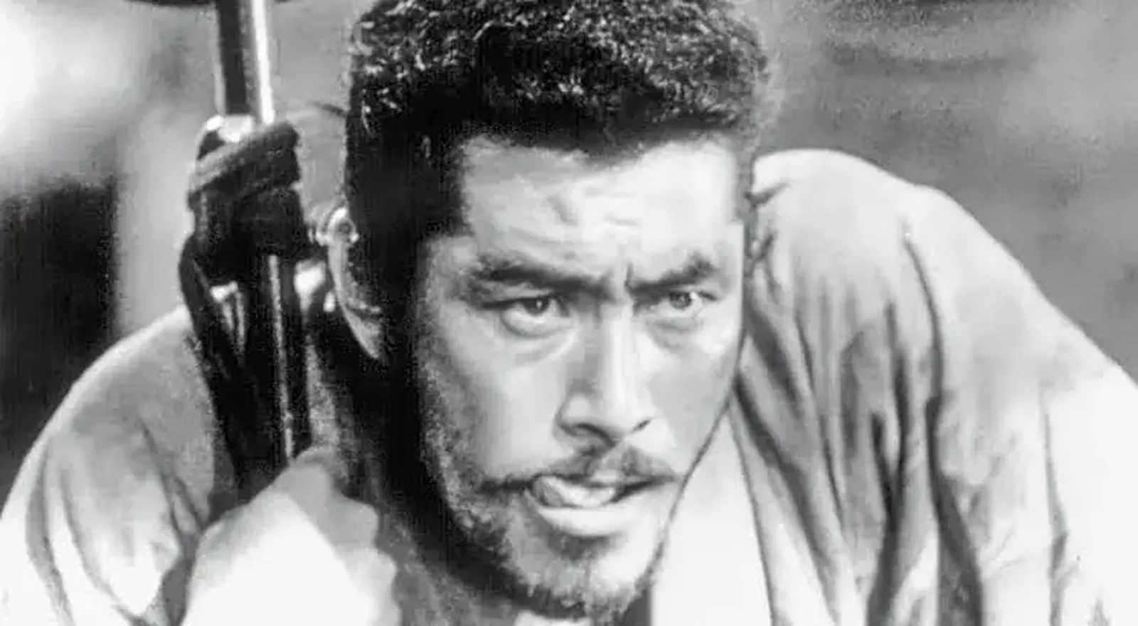 Toshiro Mifune as Kikuchiyo in Seven Samurai, in black and white, sword over his shoulder and a wild look in his eyes
